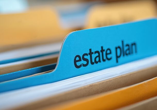 Close up of blue file folder tab labeled estate plan in office filing cabinet. Documents organize personal wealth future legacy. Secure financial records for safe keeping. Legal papers sorted for